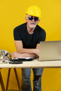 Portrait of young man using laptop while standing against yellow background