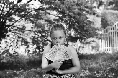 Portrait of girl holding hand fan while sitting at public park