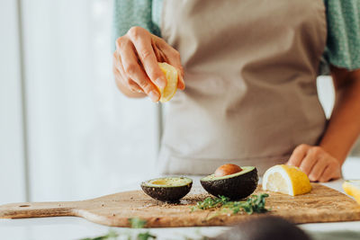 Female hands squeezing lemon on avocado while preparing healthy meal