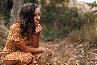 Young woman looking away while crouching in forest