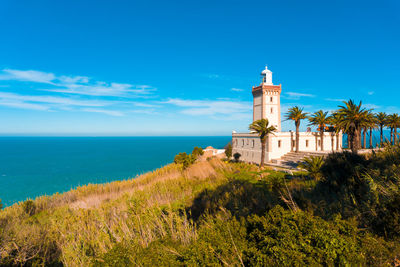 Lighthouse by sea against blue sky