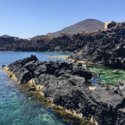 Rocks by sea against clear sky