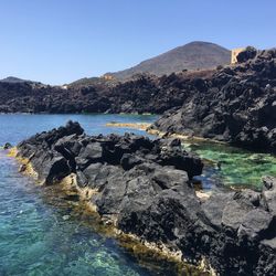 Rocks by sea against clear sky