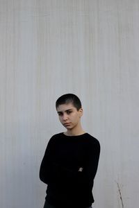 Young woman looking away while standing against wall