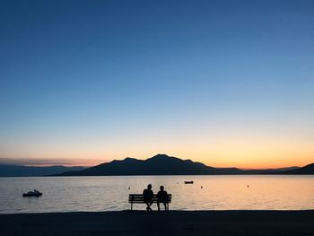 Silhouette people on beach against clear sky during sunset