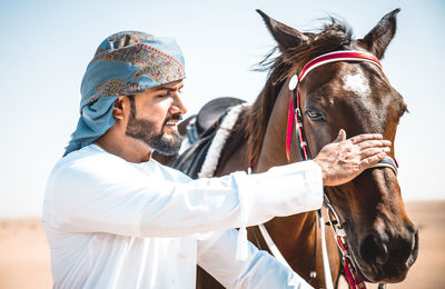 Man wearing traditional clothing standing with horse against clear sky