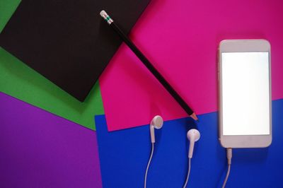 High angle view of mobile phone by headphones with pencil and book against multi colored background