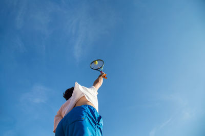 Low angle view of man playing tennis against blue sky