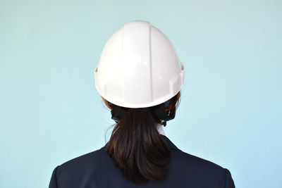 Rear view of businesswoman wearing hardhat against blue background