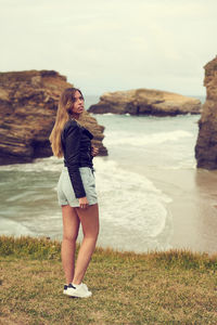 Rear view of young woman standing by sea against sky