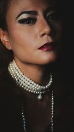 Close-up portrait of woman wearing jewelry and make-up against black background