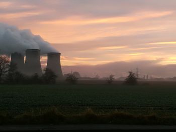 Smoke emitting from chimney on field against sky during sunset