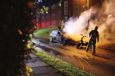 Firefighter standing by burning car in city