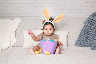 Portrait of cute baby girl sitting on sofa at home