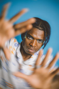 Serious african american male with braids and bright makeup looking at camera while showing blurred hands on blue background in studio