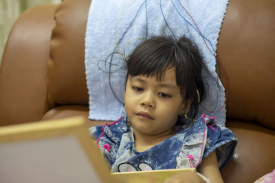 Close-up of cute girl with electrodes on head sitting on sofa at home