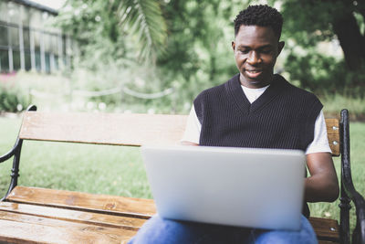 Young black man working on laptop outdoors, looking at screen, smiling