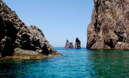 Rock formations in sea against clear blue sky