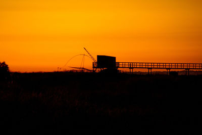 Silhouette cranes against orange sky