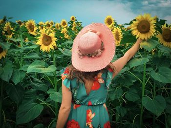 Rear view of woman wearing dress and sun hat in a field of sunflowers on a cloudy day