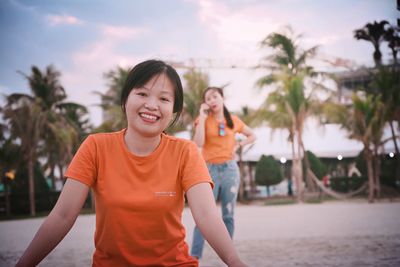 Portrait of smiling woman standing on palm trees against sky