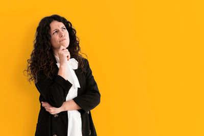 Young woman looking away while standing against yellow background