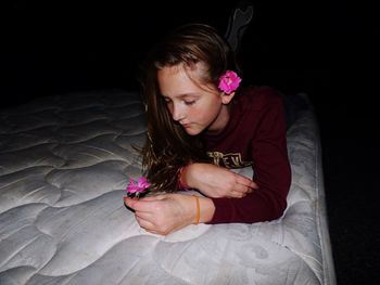 Girl holding flower while lying on bed in darkroom at home