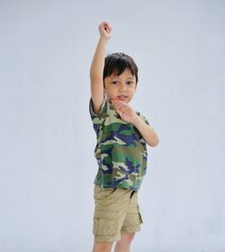 Portrait of cute boy with arm raised standing against white background