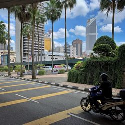 Vehicles on road by buildings in city against sky