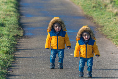 Portrait of twin brothers wearing warm clothing while standing on road