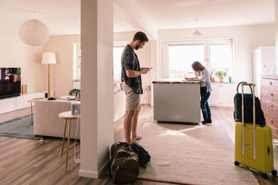 Man using mobile phone while woman filling form in apartment during vacations