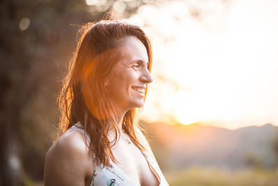 Smiling woman looking away against sky during sunset