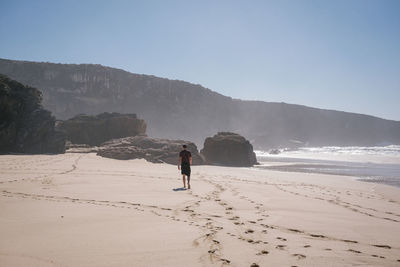 Rear view of woman walking at beach against clear sky