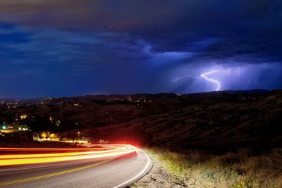 Light trails on road against dramatic sky