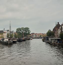 Sailboats in river by buildings against sky