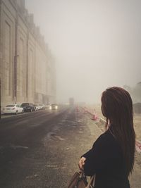 Rear view of woman on road against sky in city