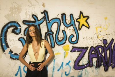 Portrait of smiling young woman standing against graffiti wall