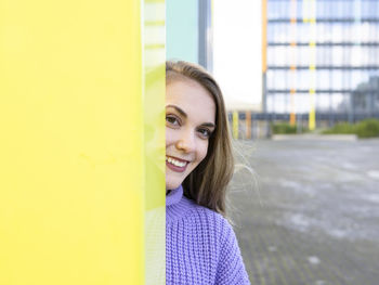 Portrait of smiling young woman against yellow wall