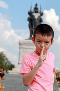 Portrait of boy with finger on lips standing against sculpture