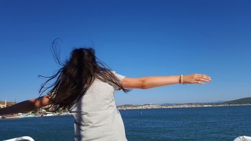 Rear view of woman with arms raised against blue sky