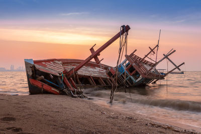 Fishing boat on beach against sky during sunset