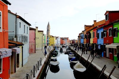 Boats moored on canal amidst buildings against sky