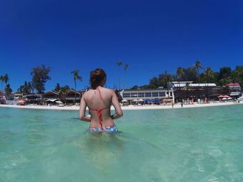 Rear view of shirtless man in swimming pool against clear blue sky