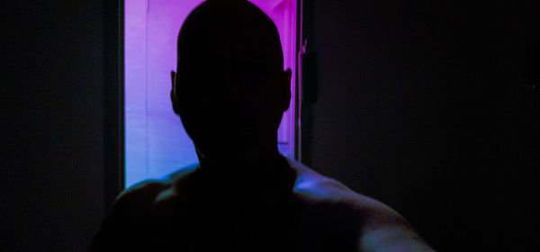 Rear view of shirtless man standing in dark room