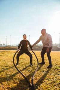 Woman exercising with rope by instructor on land against sky in sunny day