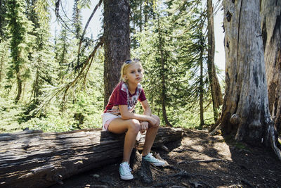 Portrait of girl sitting on log in forest