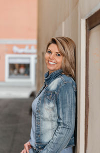 Woman in blue denim jacket and jeans smiling against urban backdrop