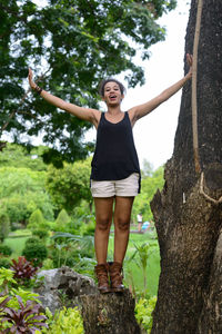 Full length of smiling young woman standing against trees