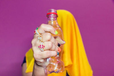 Midsection of woman holding glass bottle against pink background