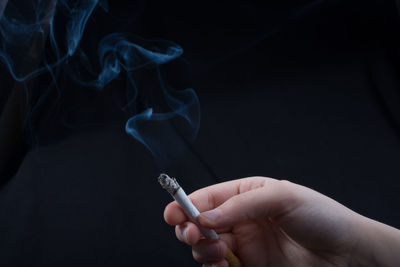 Close-up of hand holding cigarette against black background